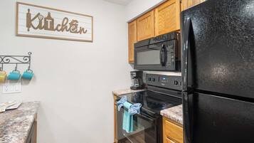 A kitchen with wooden cabinets, a black refrigerator, a microwave, and an oven.