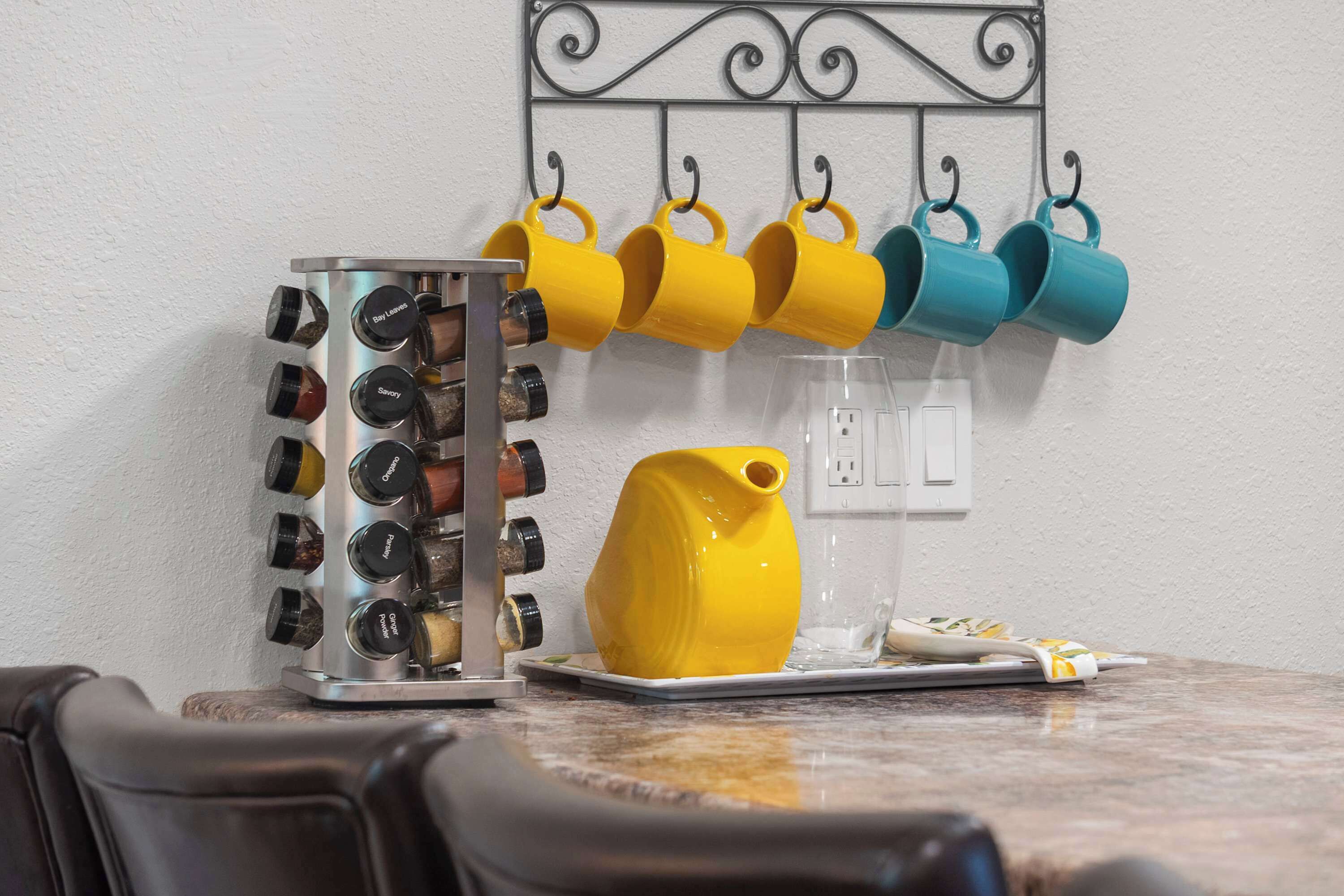 A kitchen counter with a spice rack, a yellow pitcher, and a plate with a spoon.