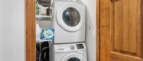 A laundry room with two stacked washing machines and a shelf with cleaning supplies.