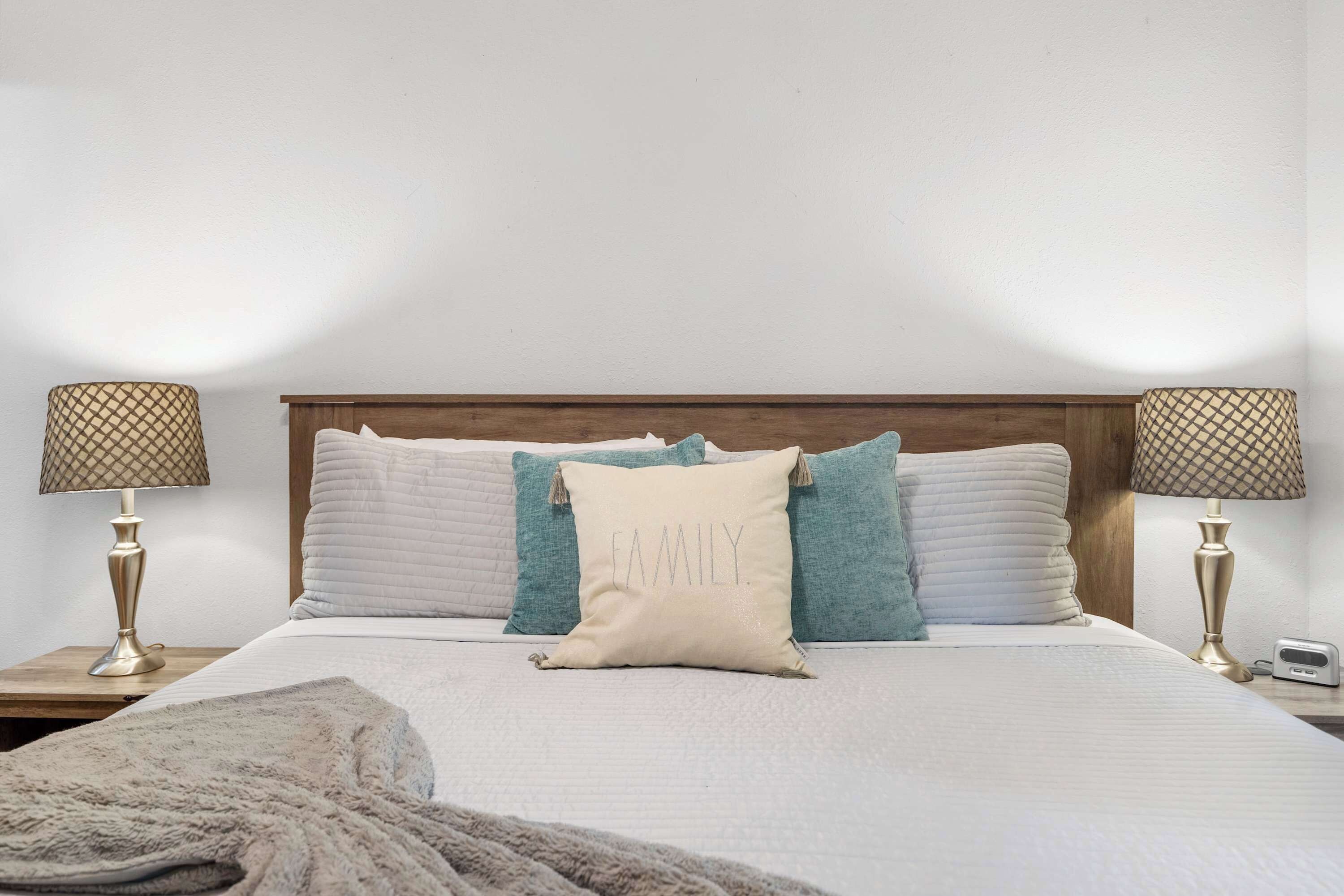 A neatly made bed with a headboard, two bedside lamps, and a pillow with "FAMILY" written on it.