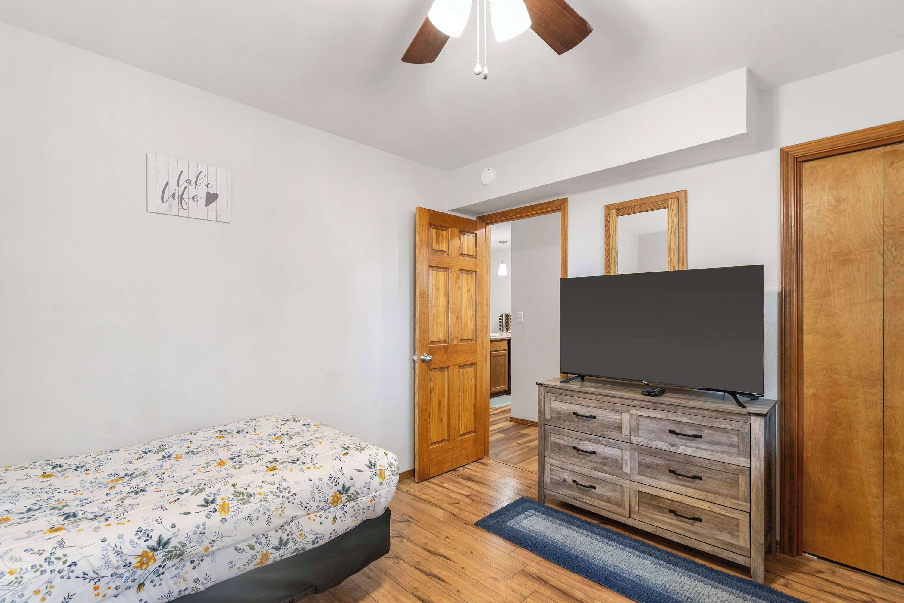 Un dormitorio con cama, cómoda, televisor y ventilador de techo.