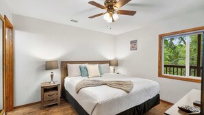 A bedroom with a bed, nightstands, a desk, a ceiling fan, and a window with a view of trees. - The Greenview Haven: Cozy For 6! (Branson West)