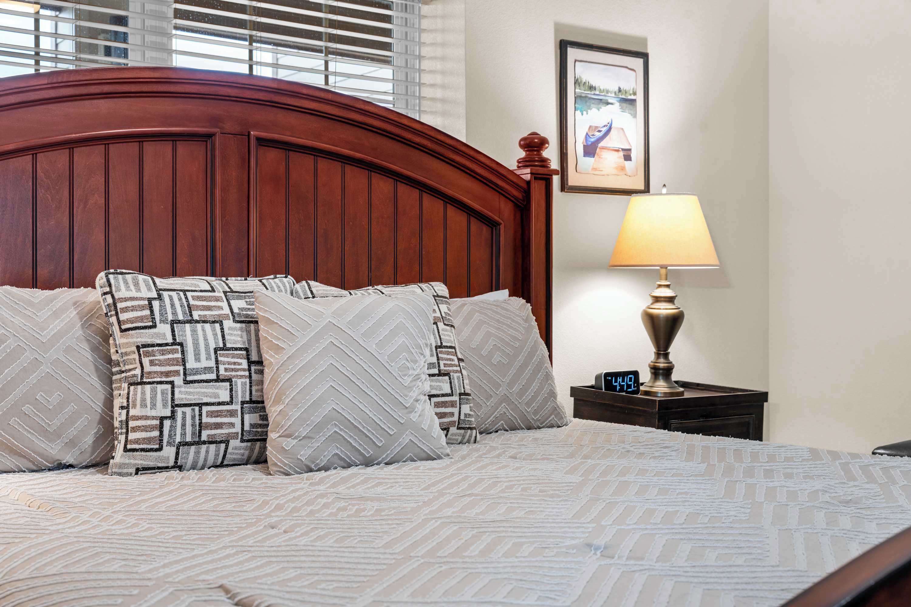 A neatly made bed with patterned pillows and a wooden headboard, a bedside lamp, and a framed picture on the wall.