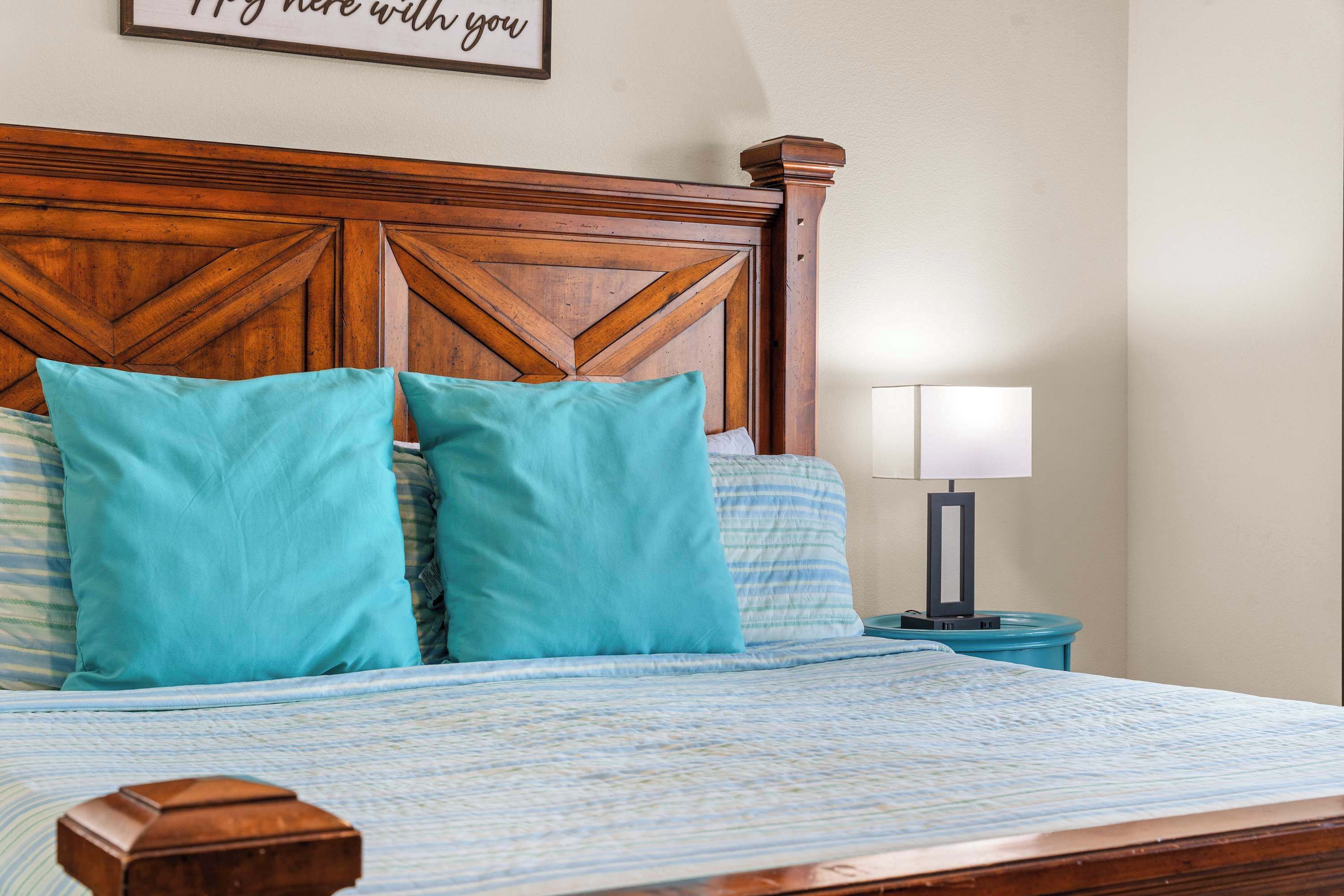 Una cama bien hecha con cabecera de madera, almohadas color turquesa y una mesita de noche con lámpara.