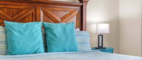 Una cama bien hecha con cabecera de madera, almohadas color turquesa y una mesita de noche con lámpara.