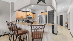 A modern kitchen with wooden cabinets, a central island with bar stools, a stainless steel refrigerator, and a black star decoration on the ceiling. - Waters Edge Retreat - For 6! (Branson)
