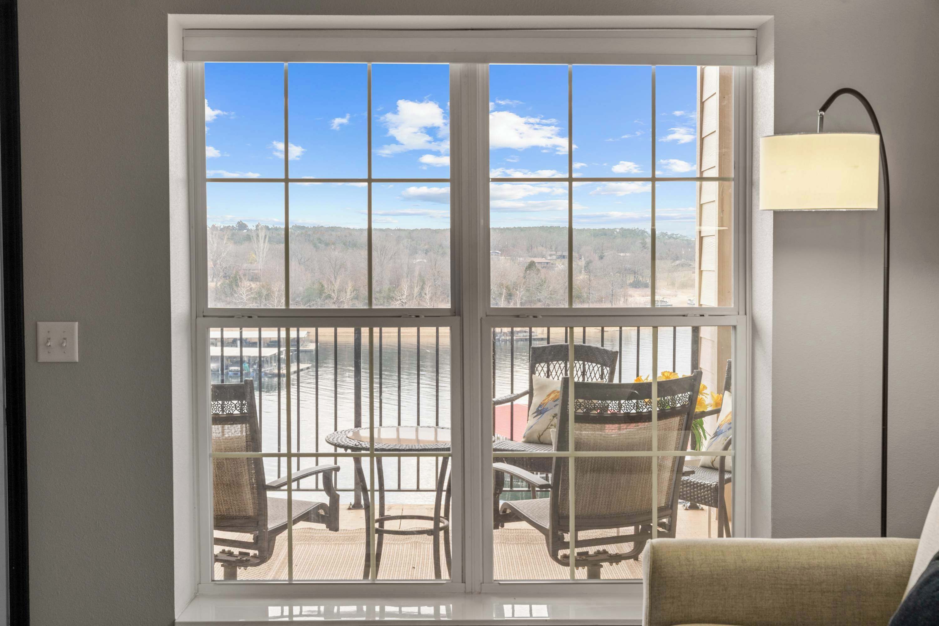 A room with a large window overlooking a body of water and a dock. There is a chair and a table inside the room.
