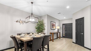 A dining area with a wooden table, dark chairs, a hanging light fixture, a potted plant, and a door in the background. - Waters Edge Retreat - For 6! (Branson)