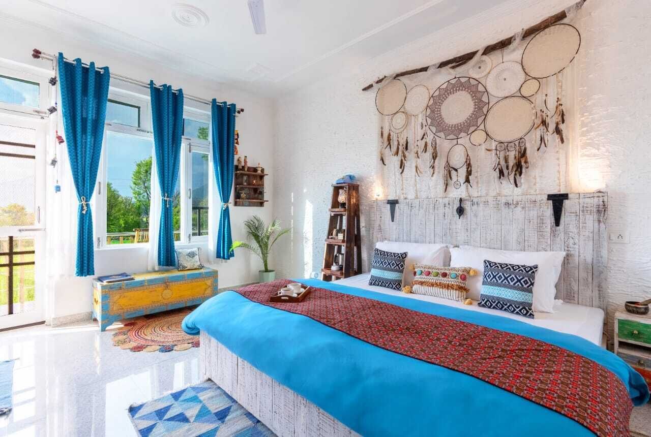 Een slaapkamer met een groot bed, blauwe gordijnen, een dromenvanger aan de muur en een houten dressoir.