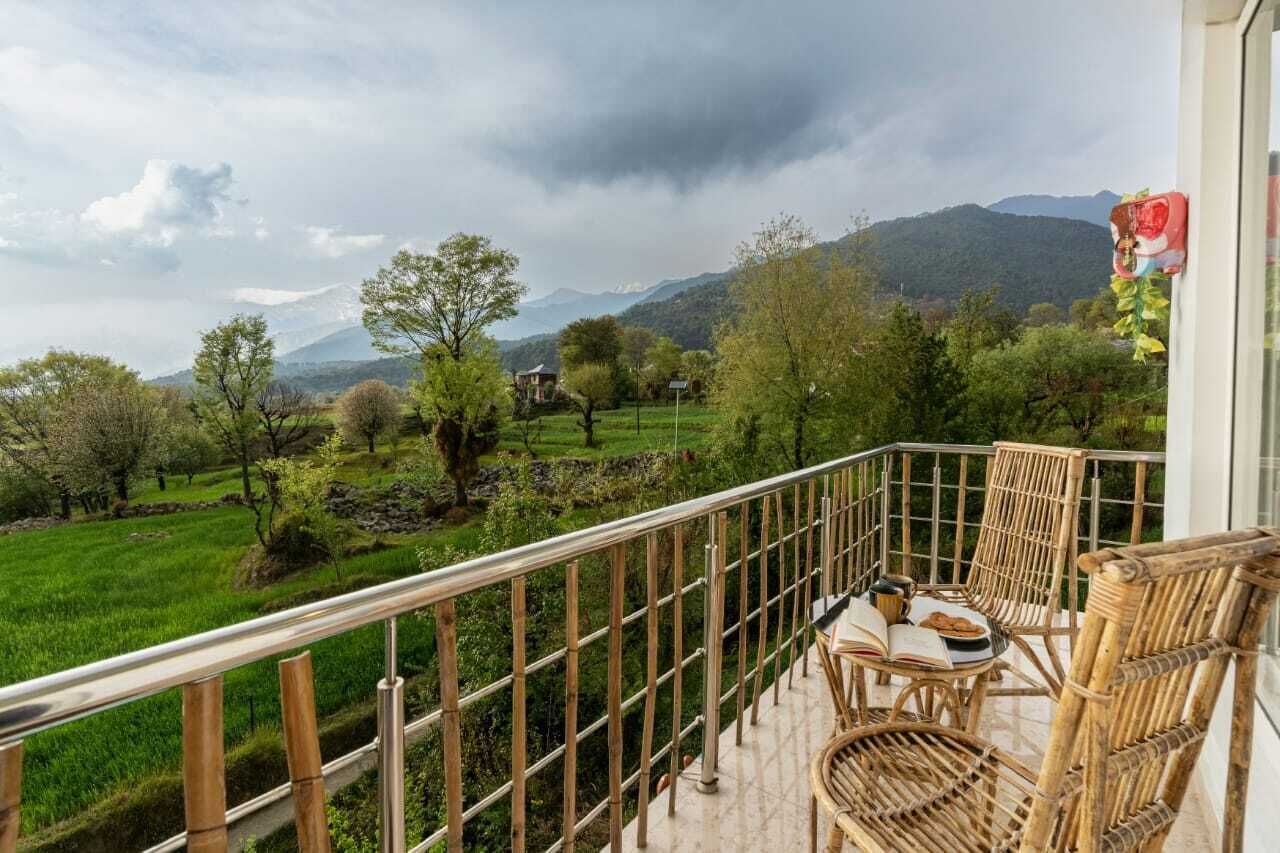 A balcony with wicker furniture, a view of a green landscape and mountains, and a red object on the railing.