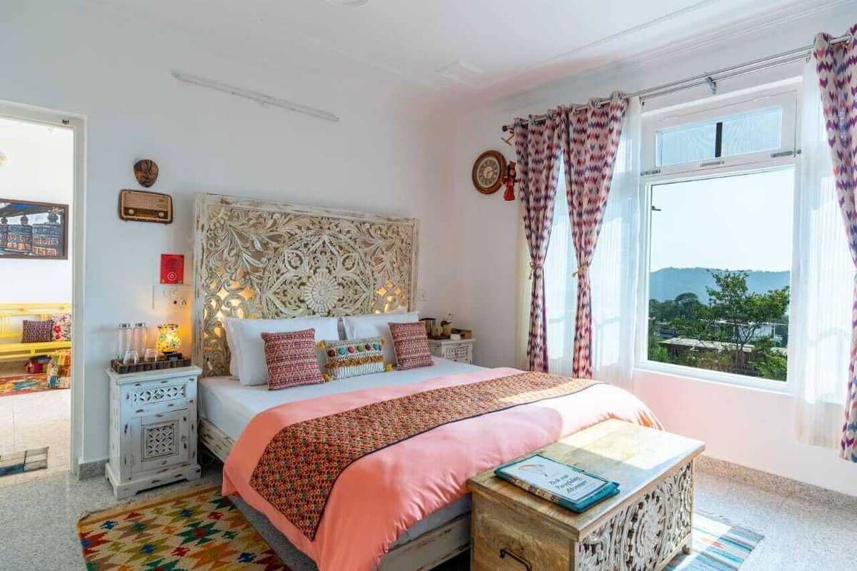 Ein Schlafzimmer mit einem großen Bett, einem Nachttisch, einer Holzkiste und einem Fenster mit Vorhängen.