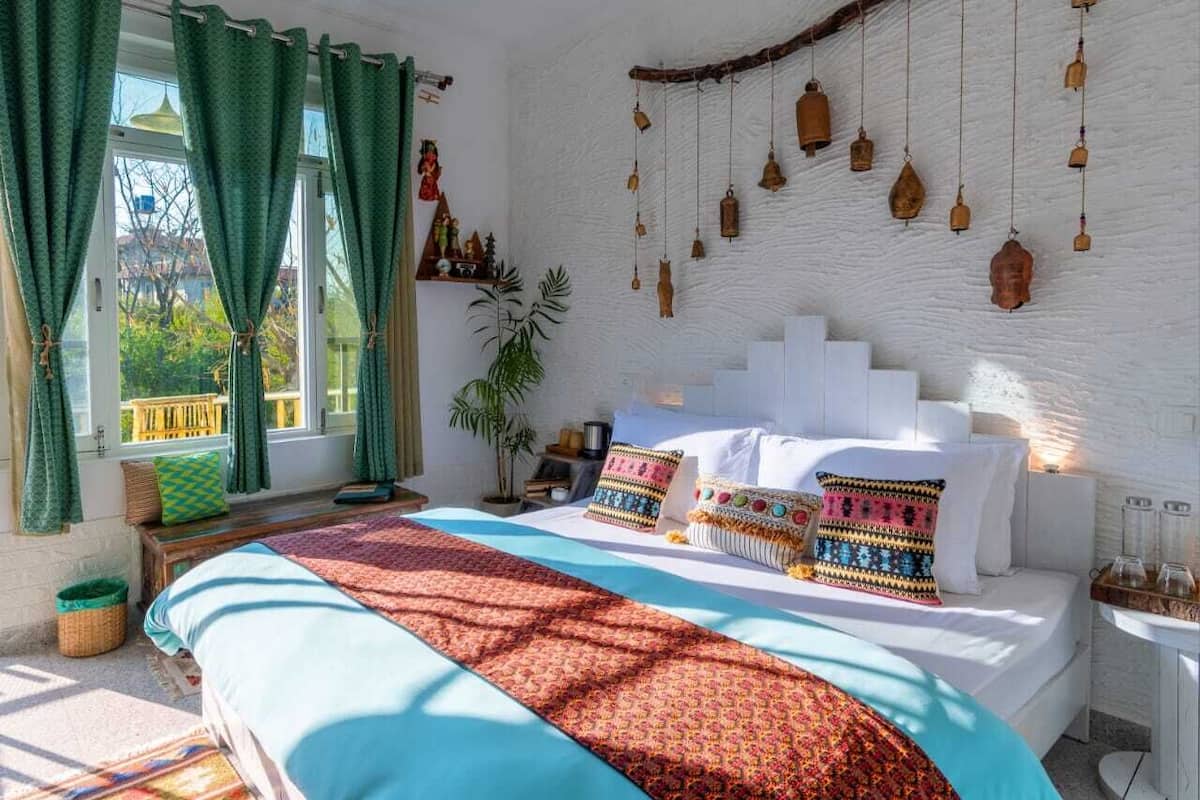 Ein Schlafzimmer mit einem großen Bett, grünen Vorhängen, einer weißen Wand und hängenden Holzglocken.