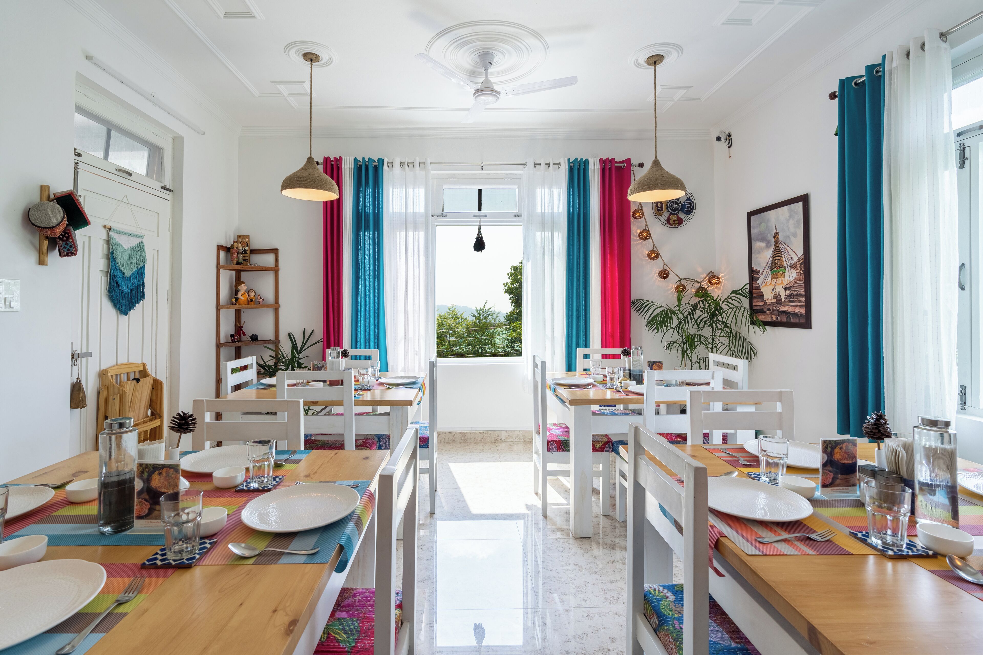 A bright dining area with white furniture, colorful table runners, and a view of greenery outside.