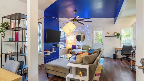 A modern living room with a blue accent wall, a ceiling fan, a sofa, a coffee table, and a bookshelf.