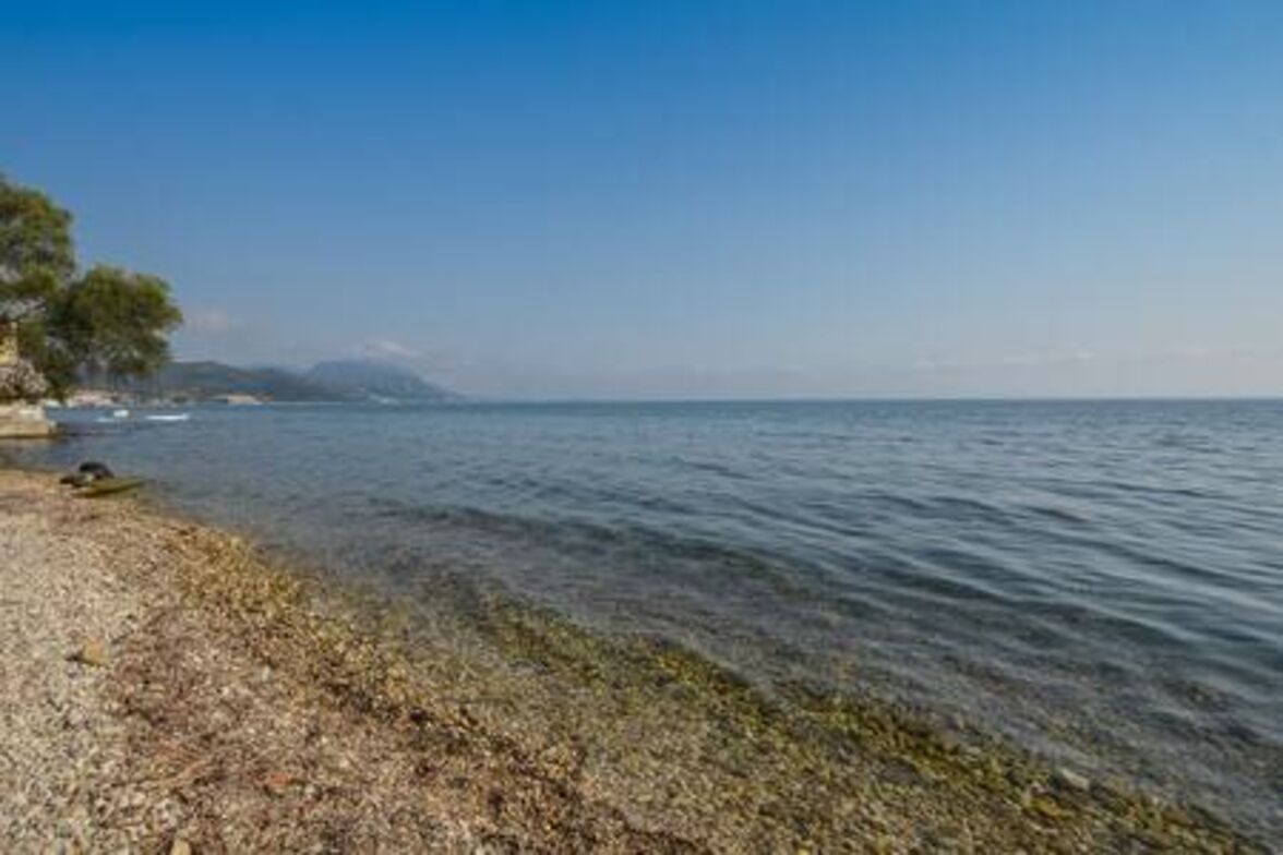 Une plage de galets avec une eau claire et une vue lointaine sur une chaîne de montagnes.