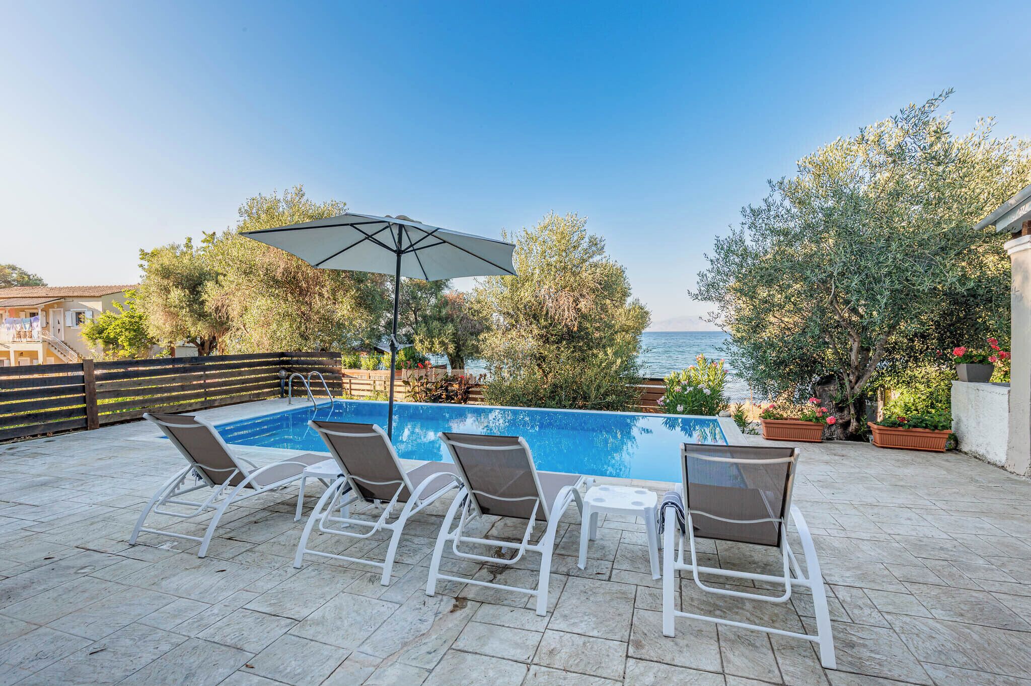 Une piscine entourée d’arbres, avec des chaises longues et un parasol, offrant une vue sur la mer.