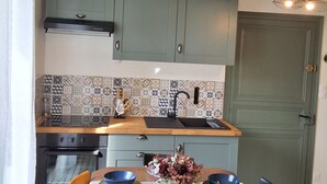 A compact kitchen with a dining area, featuring a wooden table, chairs, a built-in oven, and a sink.