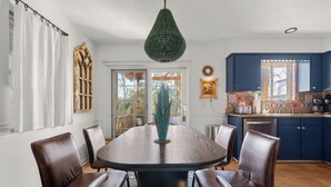 A dining area with a round table, six chairs, a decorative vase, and a green pendant light. - Abuela House with Pool - 4Bed (Columbus)