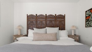 A bed with a wooden headboard, two bedside tables with lamps, and a wall with a floral painting. - Abuela House with Pool - 4Bed (Columbus)