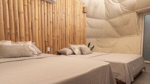 A room with two beds, a bamboo wall, and a tent-like structure.