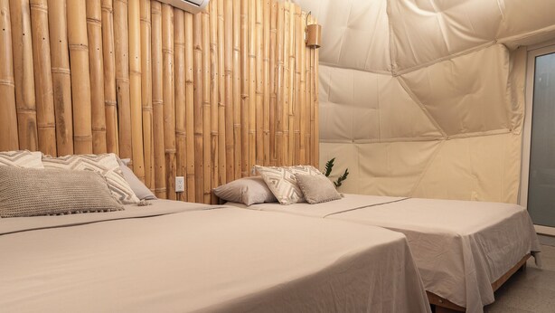 Ein Zimmer mit zwei Betten, einer Bambuswand und einer Zeltdachkonstruktion.