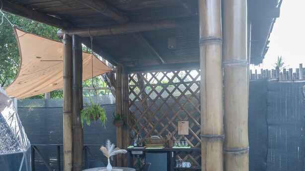 A covered outdoor area with a hot tub, bamboo columns, a table with chairs, and a lattice fence.