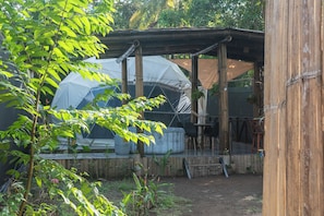 A covered outdoor area with a large transparent dome structure, wooden beams, and a seating area with chairs and a table.
