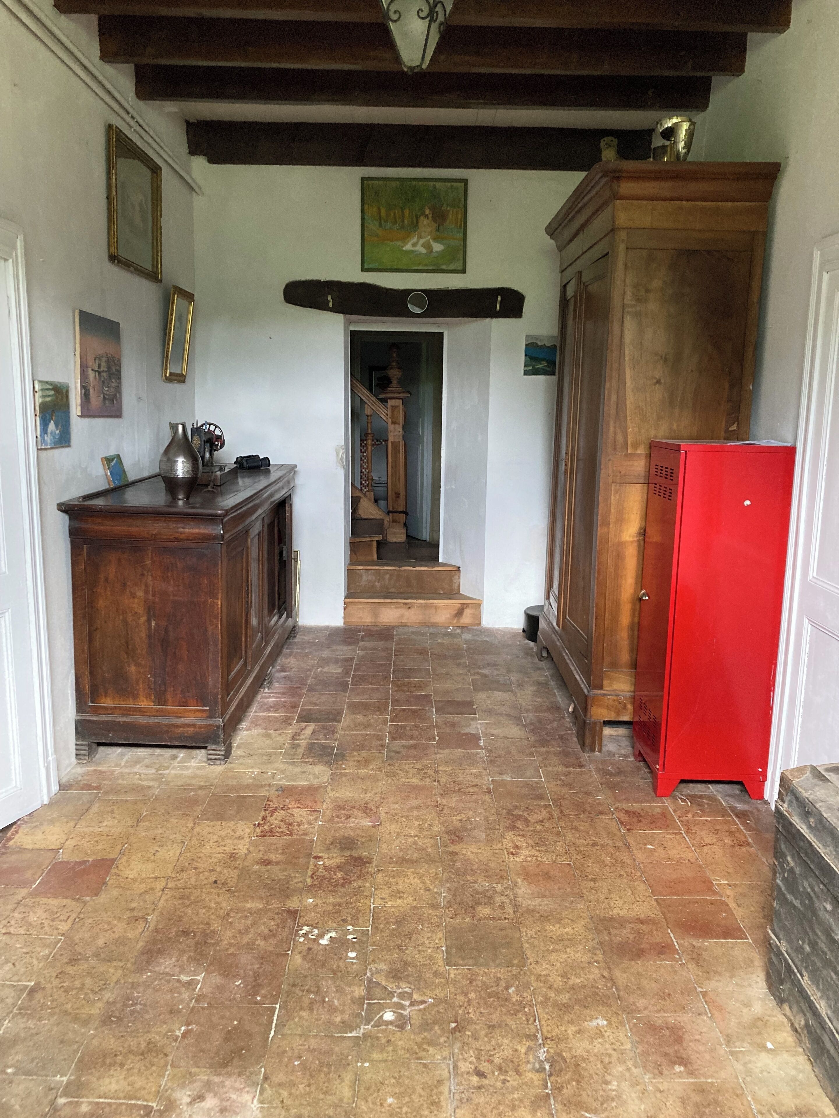 A hallway with a wooden cabinet, a red cabinet, and a staircase leading to another room.