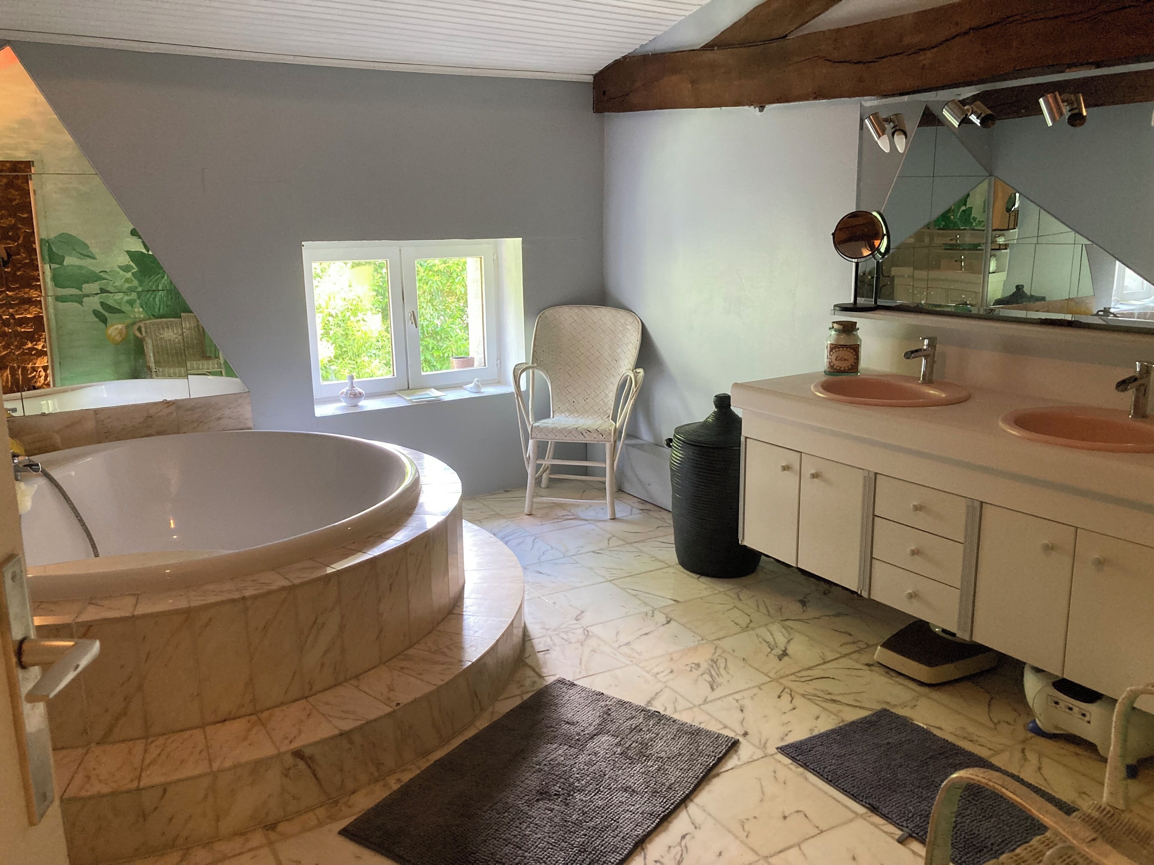 A bathroom with a freestanding bathtub, a chair, a window, and a vanity with two sinks.