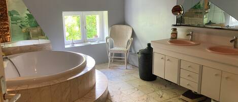 A bathroom with a freestanding bathtub, a chair, a window, and a vanity with two sinks.