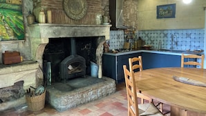 Une cuisine rustique avec une cheminée en pierre, une table à manger en bois et un mur recouvert de carreaux.