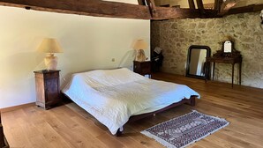 Une chambre avec un lit en bois, une table de chevet avec une lampe, un miroir et un tapis à motifs sur un plancher en bois.