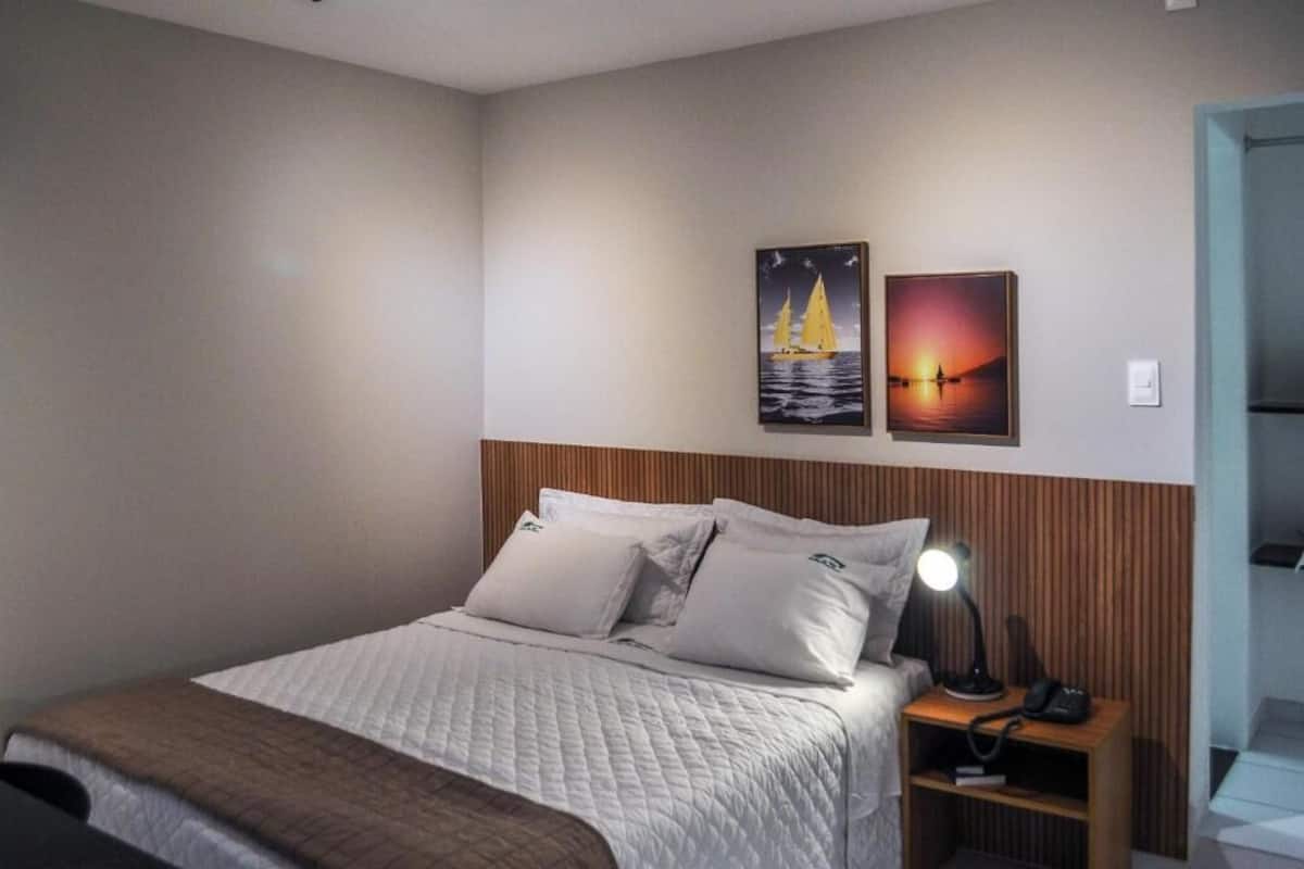 Un lit bien fait, avec une tête de lit en bois, une lampe de chevet et deux tableaux accrochés au mur.