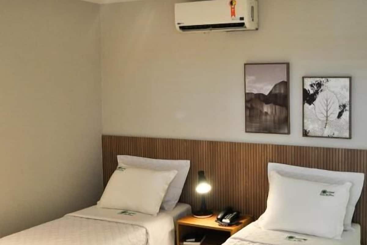 Une chambre d’hôtel avec deux lits, une table de chevet avec une lampe, un climatiseur et deux tableaux accrochés au mur.