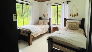 A bedroom with two beds, a ceiling fan, and a view of greenery outside. - Cozy modern house with pool and basketball court! (San Fernando de Samara)