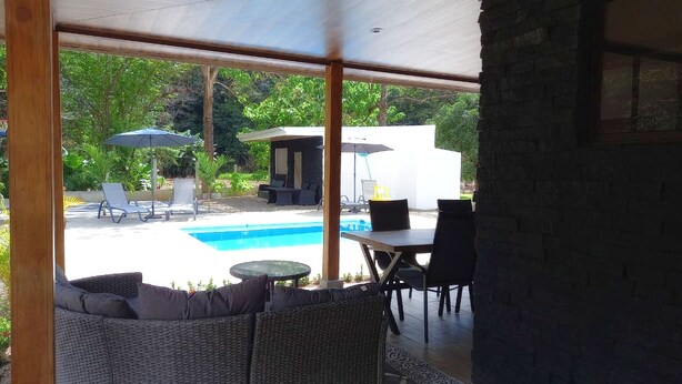 A covered outdoor area with a pool, lounge chairs, and a table. - Cozy modern house with pool and basketball court! (San Fernando de Samara)