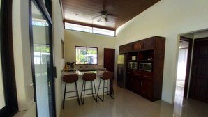 A modern kitchen with a bar area, wooden cabinets, and a ceiling fan. - Cozy modern house with pool and basketball court! (San Fernando de Samara)