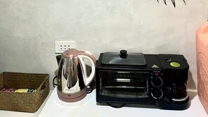 A kitchen with a microwave, coffee maker, kettle, and a basket of snacks.