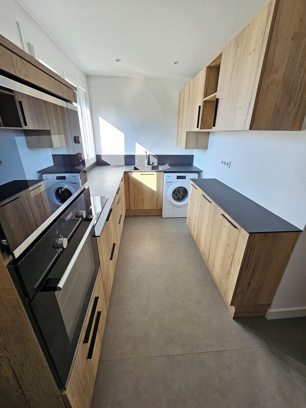 A modern kitchen with wooden cabinetry, a built-in oven, a washing machine, and a countertop with a sink.