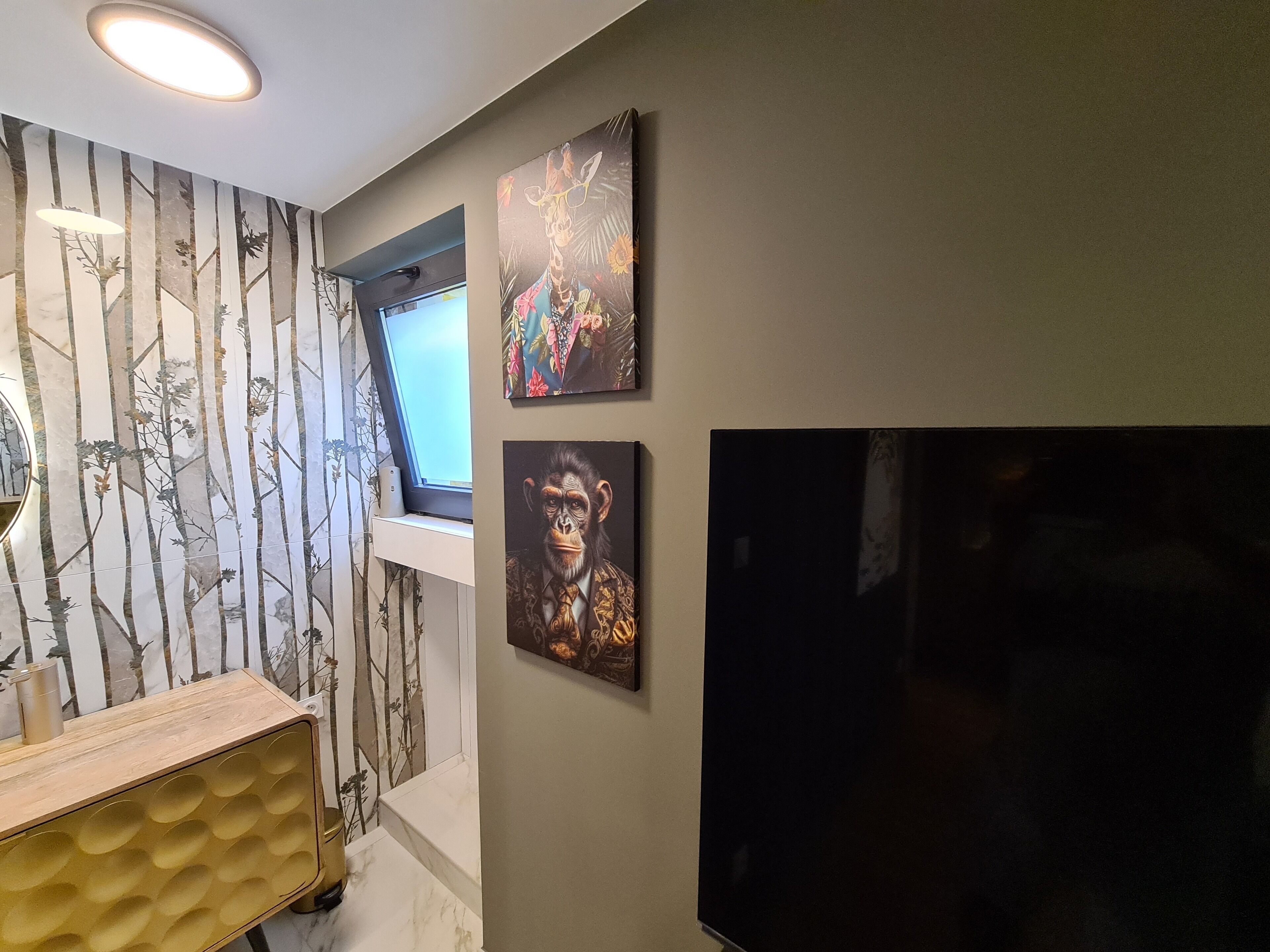 Ett rum med en stor tv-skärm, ett konsolbord i trä och en vägg med en tapet med skogsmotiv samt två inramade konstverk.