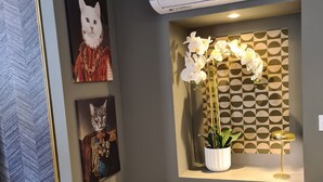 Una sala de estar moderna con pared gris, aire acondicionado instalado, un sillón azul y decoración de pared que incluye un gato y un perro.