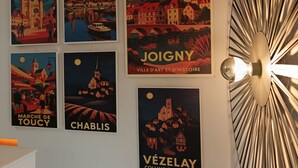 Una pared con seis carteles de pueblos franceses, un accesorio de iluminación moderno y un armario blanco.