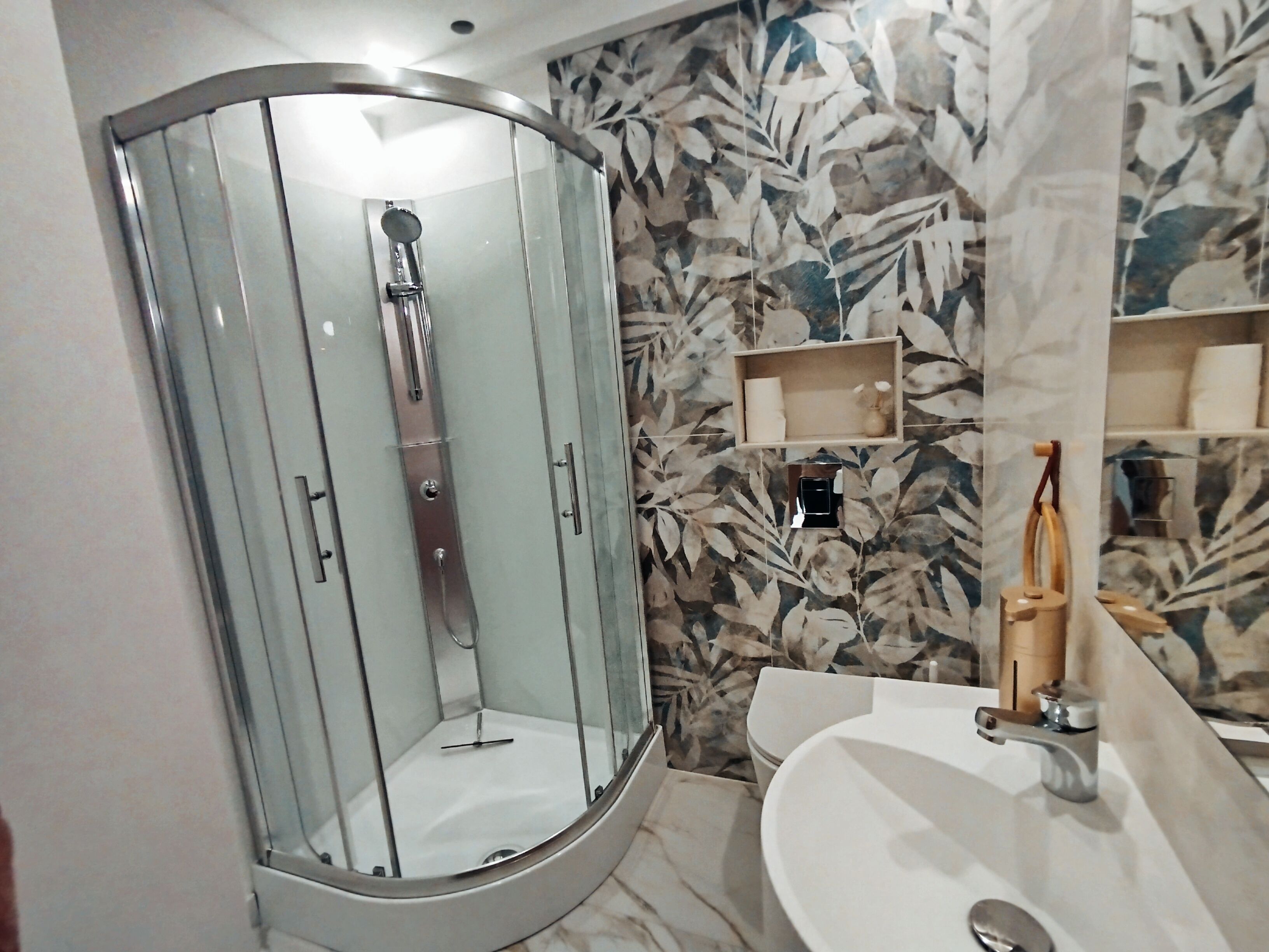 Ein modernes Badezimmer mit einer gläsernen Duschkabine, einem weißen Waschbecken und einem Marmorboden.