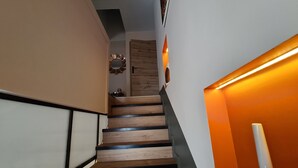 Una escalera con peldaños de madera y barandillas negras, que conduce a una habitación con una puerta de madera y un espejo en la pared.