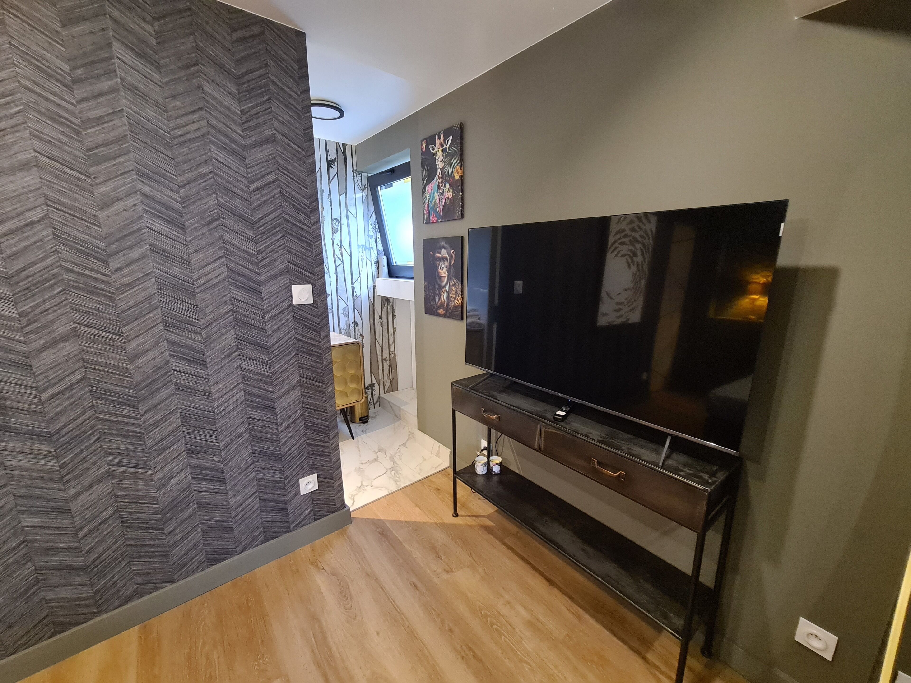 A modern living room with a large flat-screen TV, a dark wooden entertainment unit, and a herringbone-patterned wall.