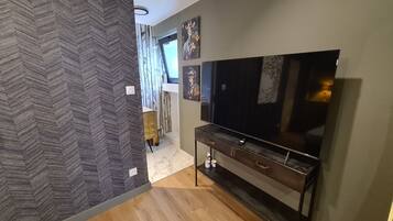 A modern living room with a large flat-screen TV, a dark wooden entertainment unit, and a herringbone-patterned wall.