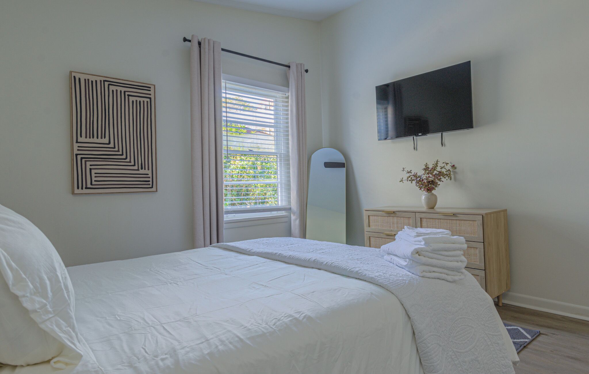 A bedroom with a bed, a TV, a mirror, a dresser, and a window with curtains.