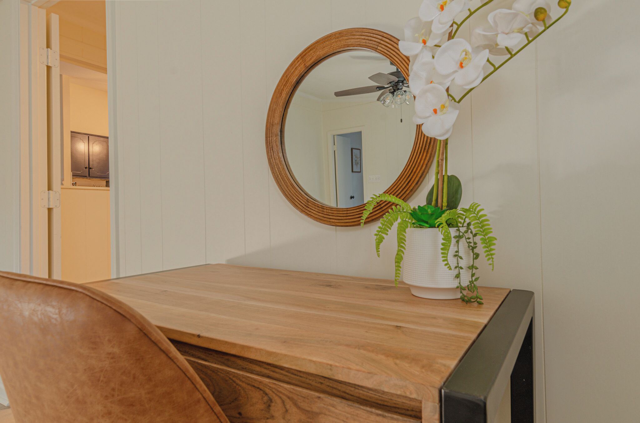 Une table à manger en bois, avec un miroir au-dessus, une plante en pot et une chaise.