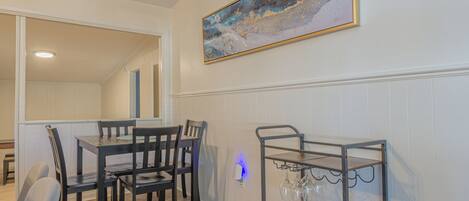Un comedor con una mesa y sillas de madera, una lámpara fijada a la pared y una estantería para vinos.