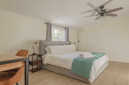 A bedroom with a bed, a desk, a chair, a ceiling fan, and a window with curtains.